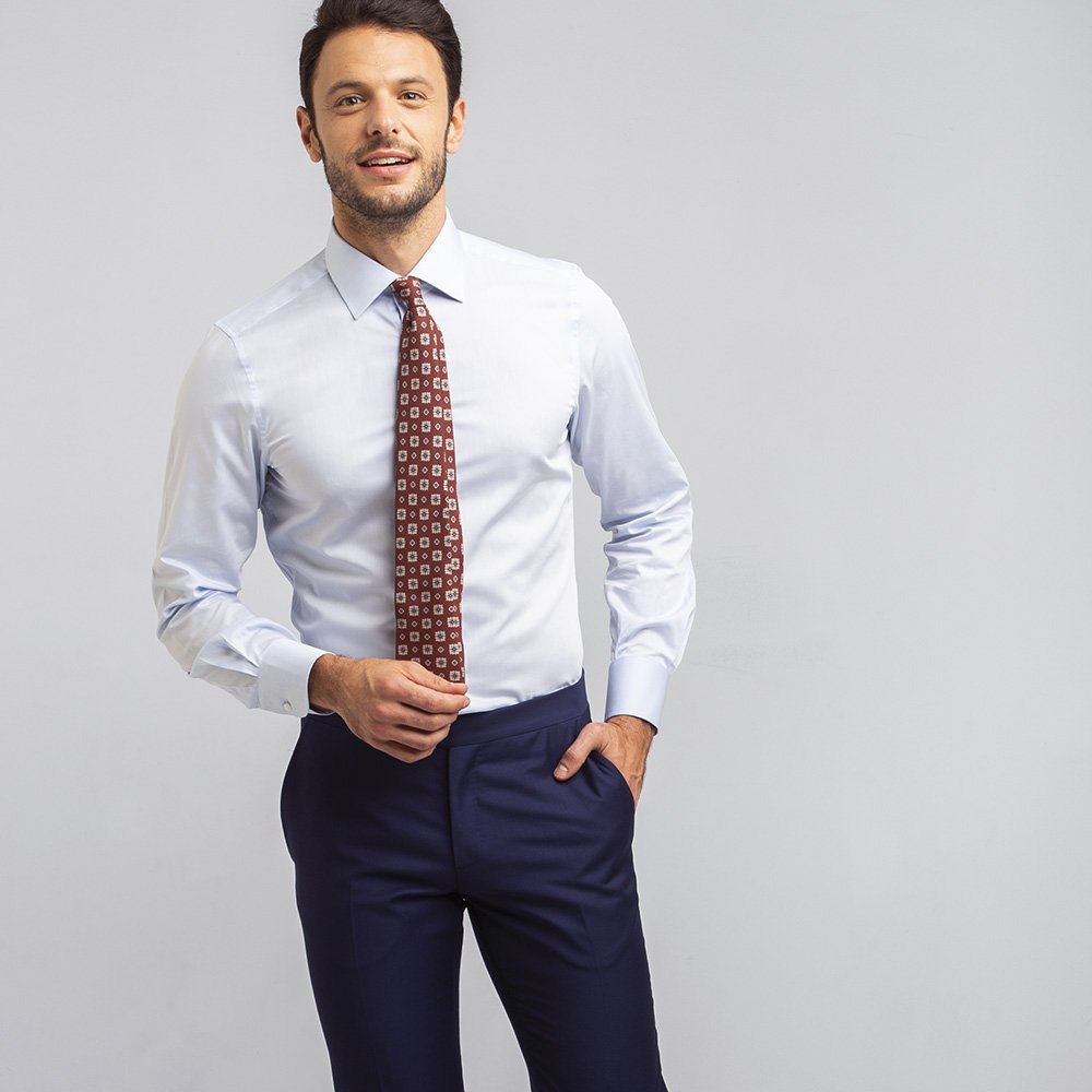 Un uomo indossa una camicia eco azzurra in cotone biologico, cravatta fantasia bordeaux e pantaloni blu.