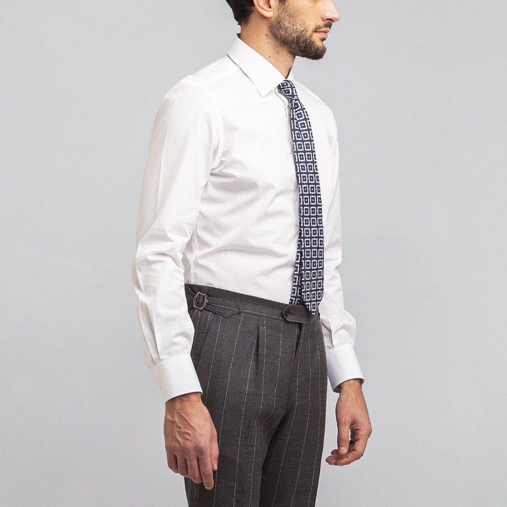 Un uomo indossa una camicia traveller bianca, cravatta fantasia e pantaloni grigi gessati.