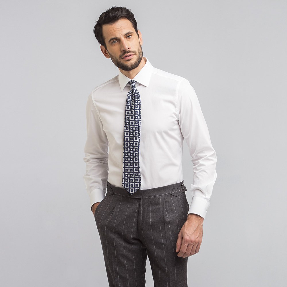 Un uomo indossa una camicia icon bianca popeline, cravatta fantasia e pantaloni grigi gessati.