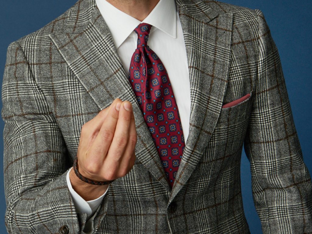Dettaglio su una giacca da uomo principe di galles, camicia bianca e pochette coordinata con la cravatta