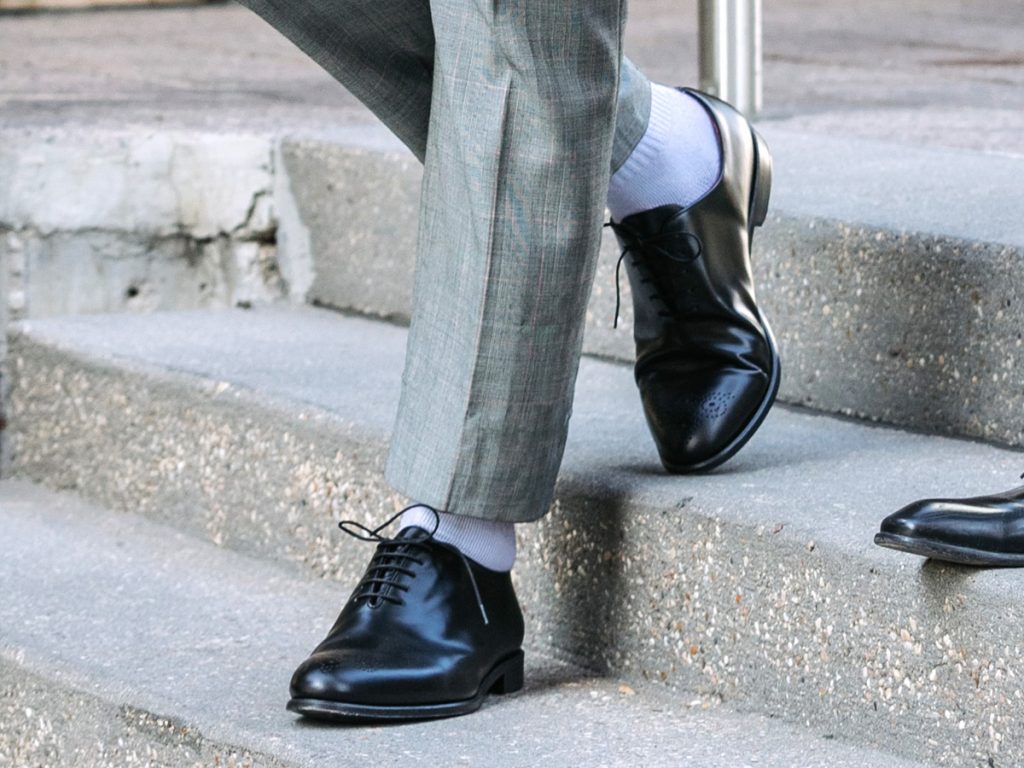 Dettaglio sui calzini bianchi indossati con un paio di scarpe nere eleganti e pantaloni principe di galles