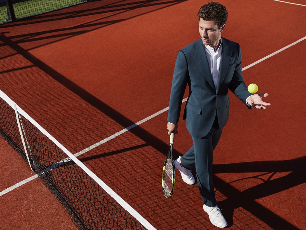 A man dressed in an elegant suit plays on a tennis court